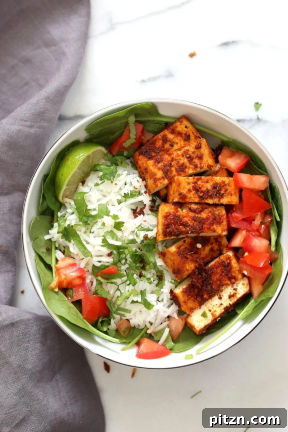 A beautifully assembled Cajun Tofu Bowl from a top-down perspective, showcasing the golden-baked tofu, fluffy cilantro lime rice, fresh greens, and diced tomatoes, ready to be enjoyed.