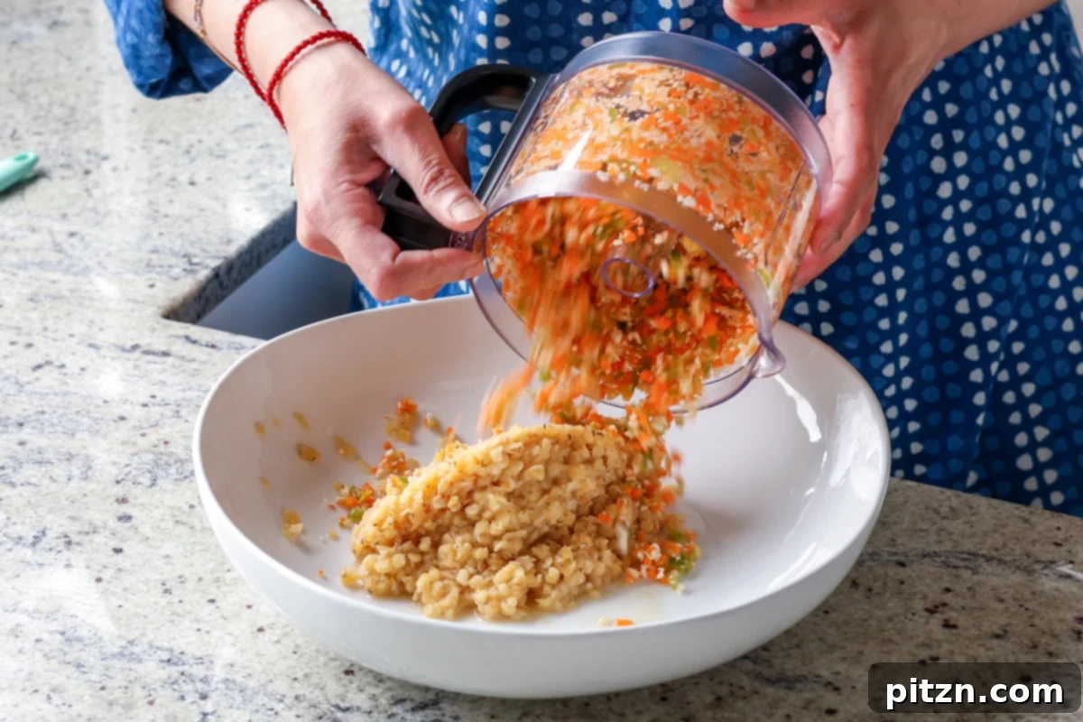 Finely chopped vegetables from the food processor being added to a bowl of cooked red lentils, ready for mixing into the burger patties.