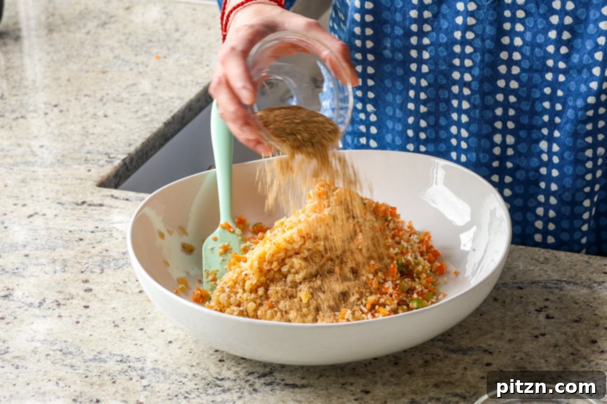 Adding dried spices like chipotle powder and onion flakes to the lentil and vegetable burger mixture in a bowl.