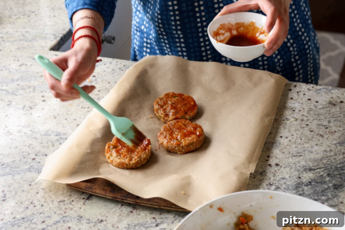 Brushing the BBQ glaze onto raw lentil burger patties arranged on a baking sheet before baking, ensuring rich flavor.