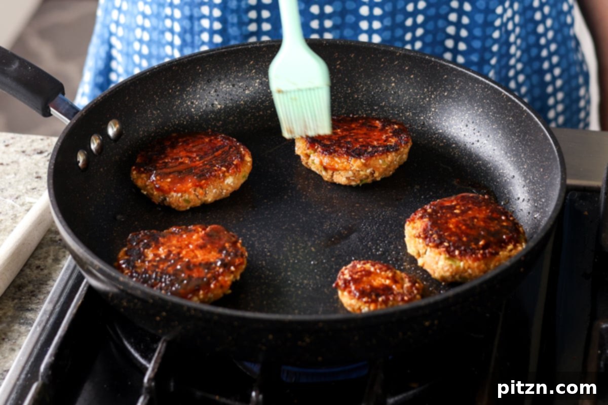 Brushing additional BBQ sauce onto the pan-frying lentil burgers, adding a final layer of smoky flavor and a glossy finish.
