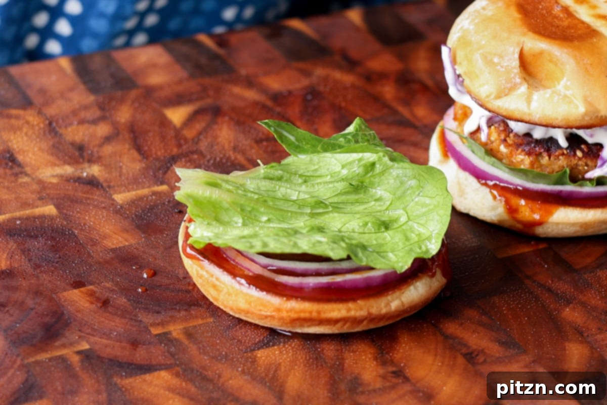 Fresh lettuce and juicy tomato slices arranged on a toasted bun, forming the base for a BBQ lentil burger.