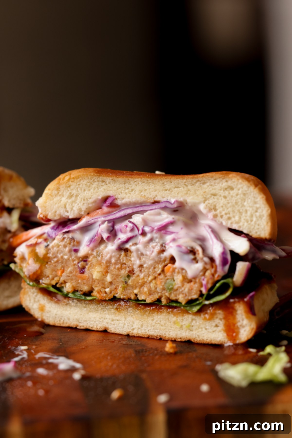 A BBQ lentil burger sliced in half, revealing the rich, textured interior of the patty, alongside layers of fresh toppings.