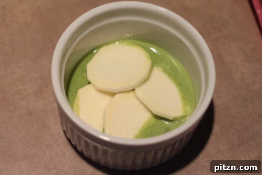 spinach alfredo sauce and white sweet potatoes being layered in a small white casserole dish