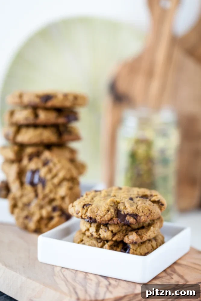 Pistachio cookies on white plate with stack of vegan cookies in background on wooden board