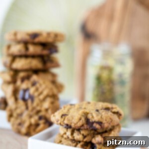Pistachio cookies on white plate with stack of vegan cookies in background on wooden board