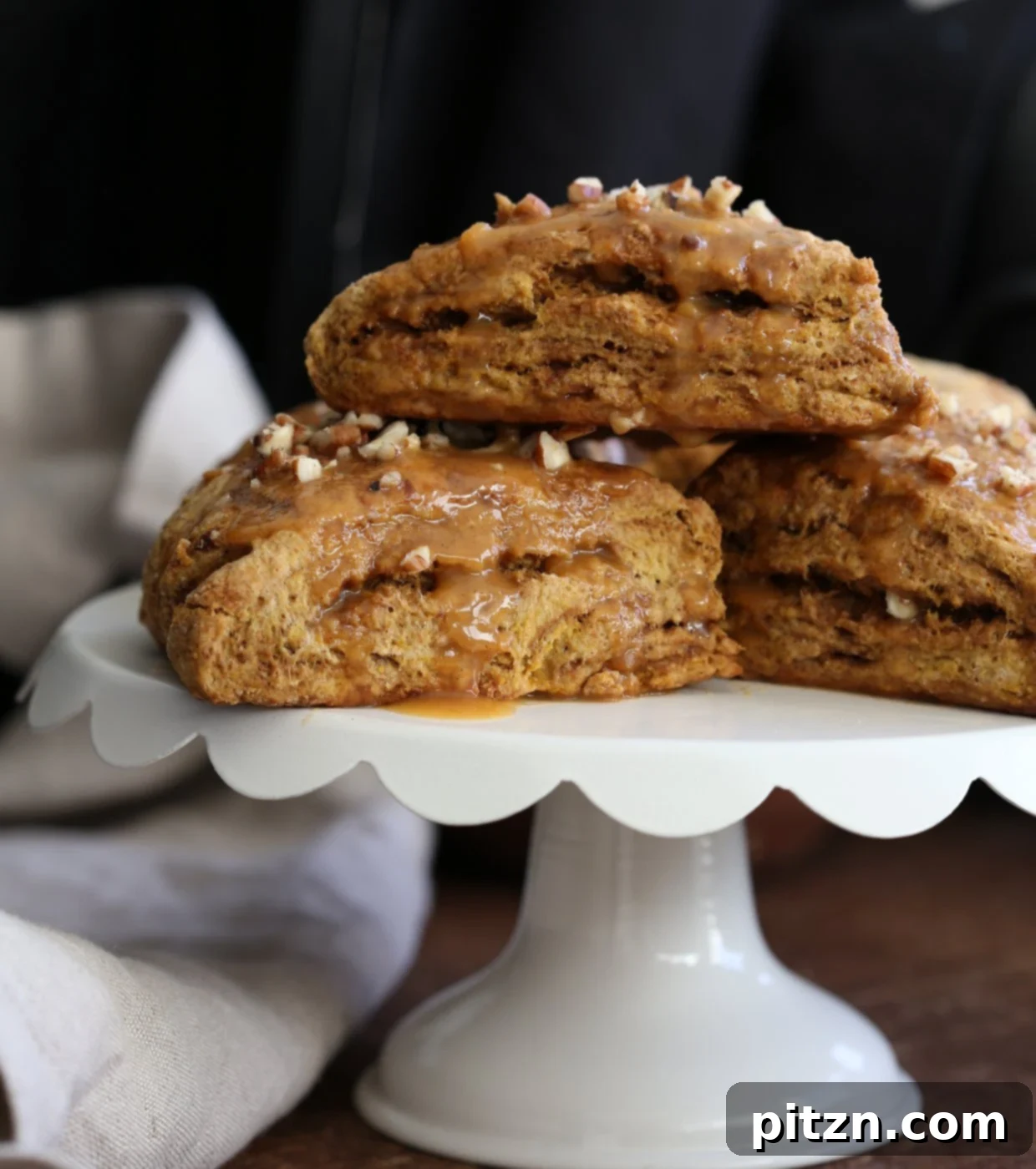 Beautifully glazed vegan pumpkin scones with chopped pecans on a rustic wooden board