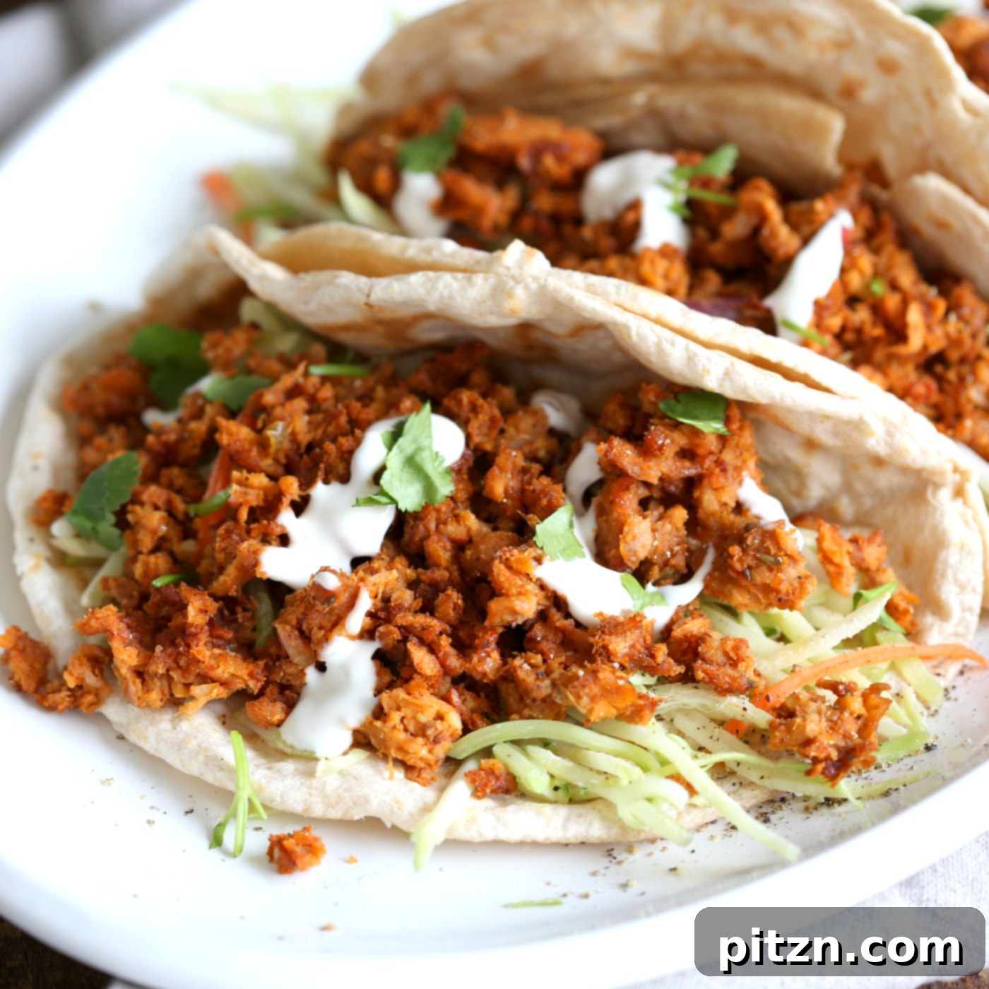 A vibrant close-up of Mango BBQ Soy Curls piled high in a taco shell, accompanied by a fresh, creamy slaw. This vegan, gluten-free, and oil-free dish offers a delightful balance of sweet, smoky, and tangy flavors.