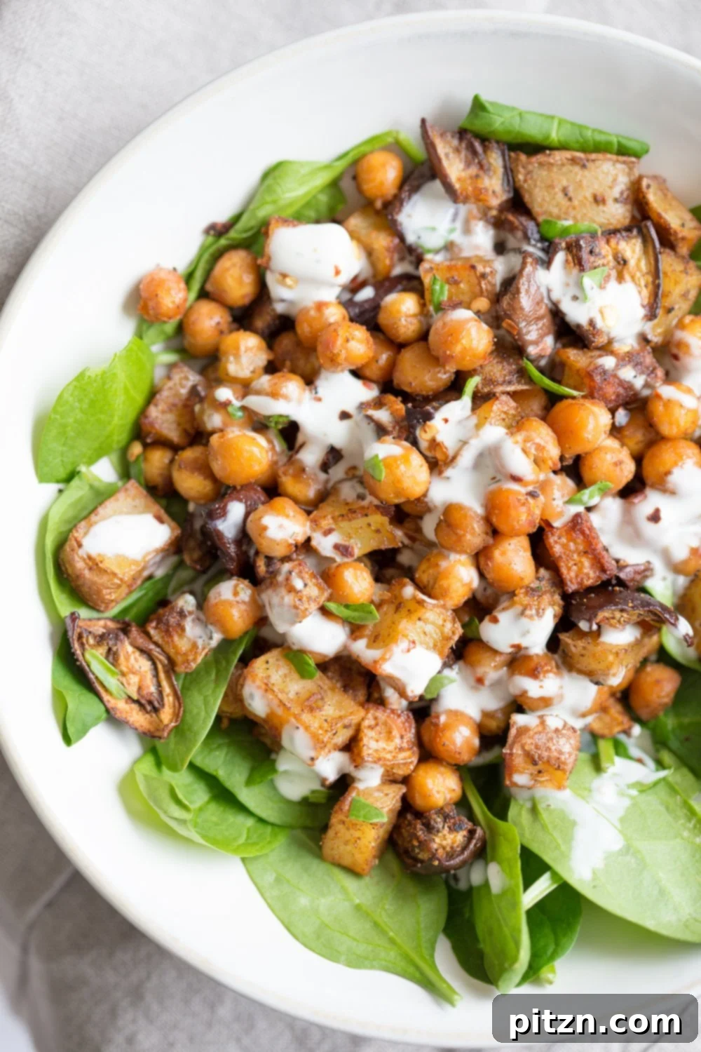 A vibrant bowl of Moroccan Merguez roasted vegetables and chickpeas, garnished with fresh parsley and a side of creamy tahini dressing. VeganRicha.com