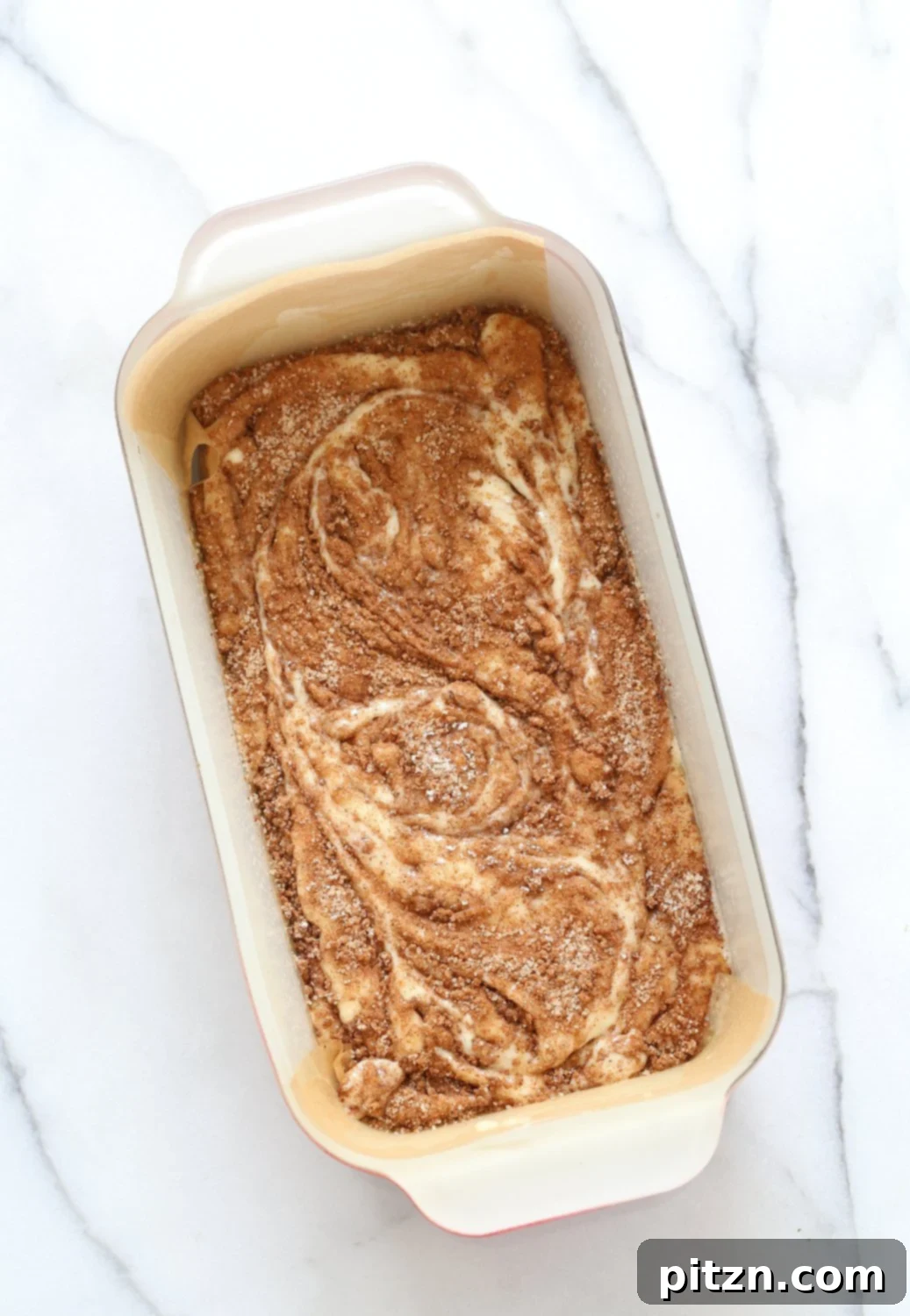 Irresistible Vegan Cinnamon Swirl Cake 8 The layering process of the Vegan Cinnamon Swirl Cake, with half the batter spread in a loaf pan and a generous sprinkle of cinnamon sugar over it. An essential step for delicious swirls.