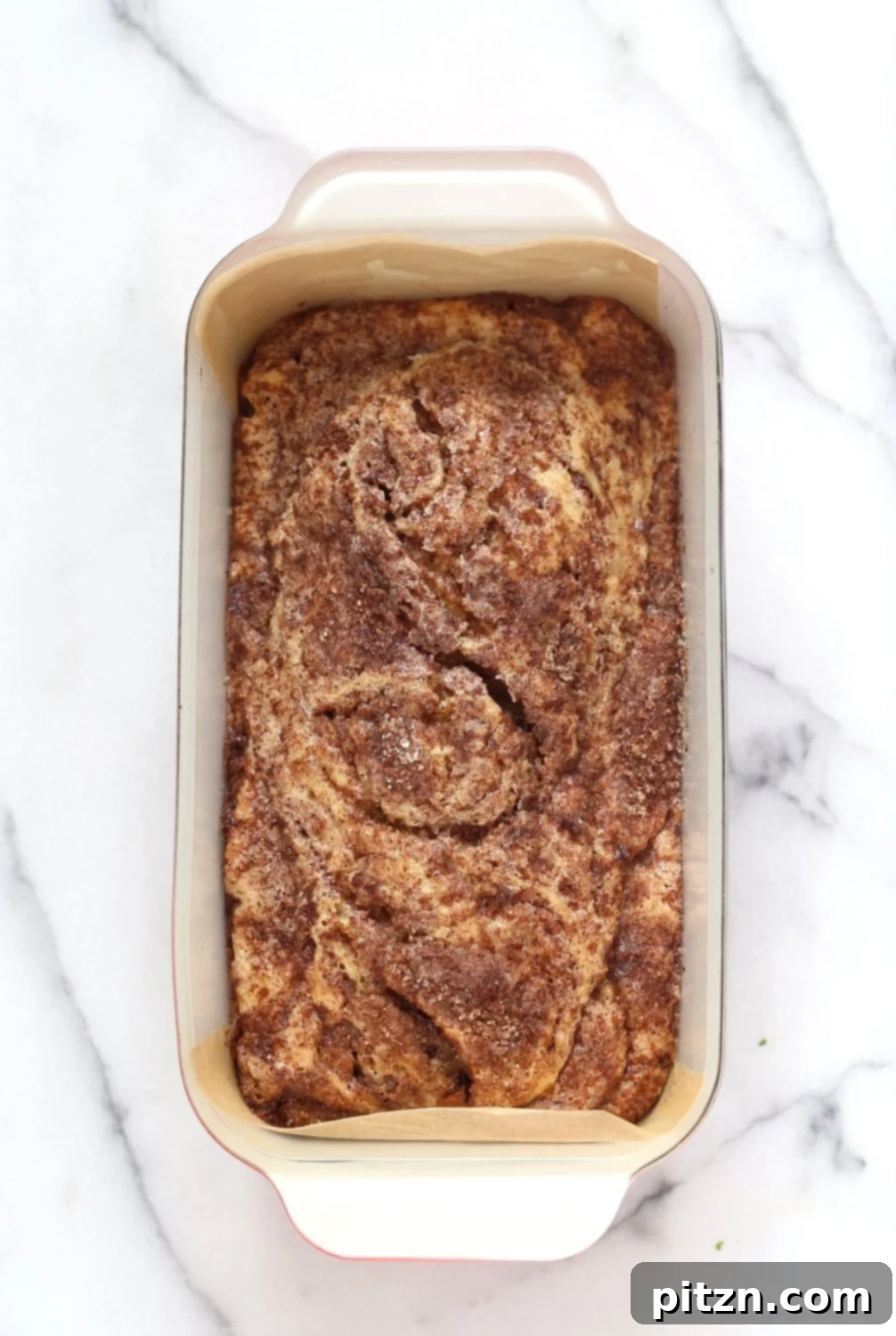 Irresistible Vegan Cinnamon Swirl Cake 9 The second layer of batter being spread over the cinnamon sugar, followed by more cinnamon sugar and a final swirl with a knife, creating the iconic Vegan Cinnamon Swirl Cake pattern.