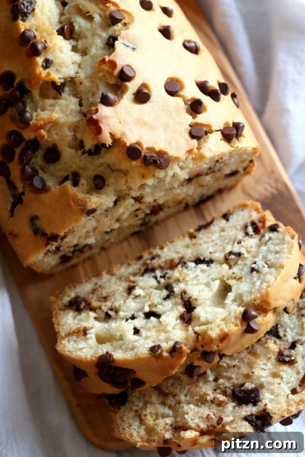 Decadent Vegan Chocolate Chip Cake 3 Close-up top shot of a freshly baked Vegan Chocolate Chip Quick Bread on a rustic wood board, highlighting its golden crust and melted chocolate chips.
