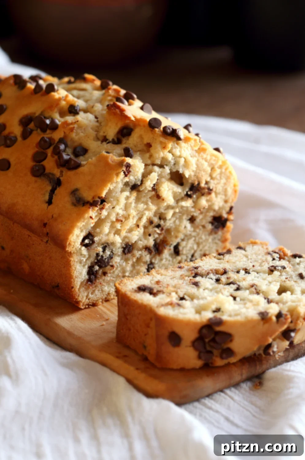 Decadent Vegan Chocolate Chip Cake 9 A perfectly baked loaf of Vegan Chocolate Chip Cake resting on a white napkin over a wooden table, showcasing its golden crust.