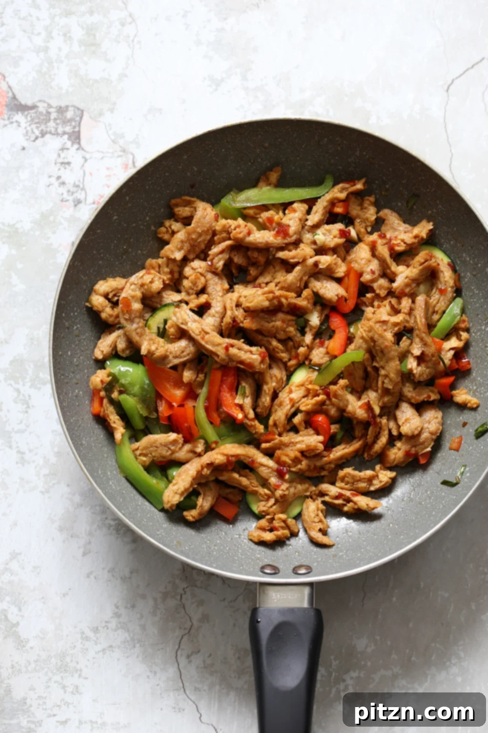 Crispy Vegan General Tso's Soy Curls 4 Soy curls and vegetables cooking in a grey skillet with General Tso's sauce