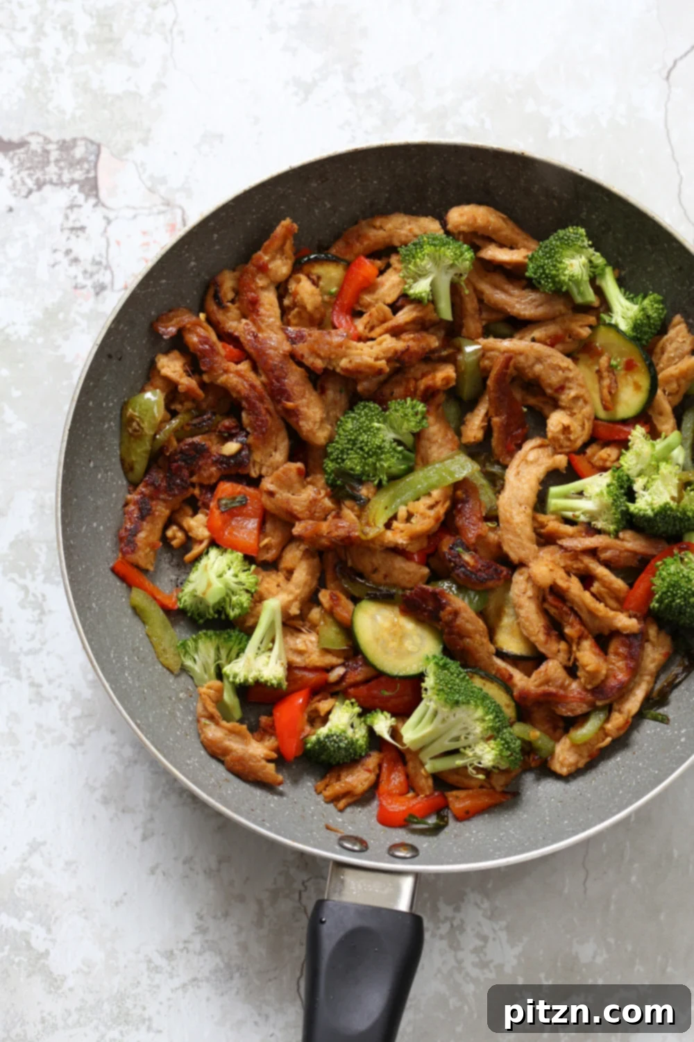 Crispy Vegan General Tso's Soy Curls 5 Close-up of vegan General Tso Soy curls and vegetables in a grey skillet, coated in thick, glossy sauce