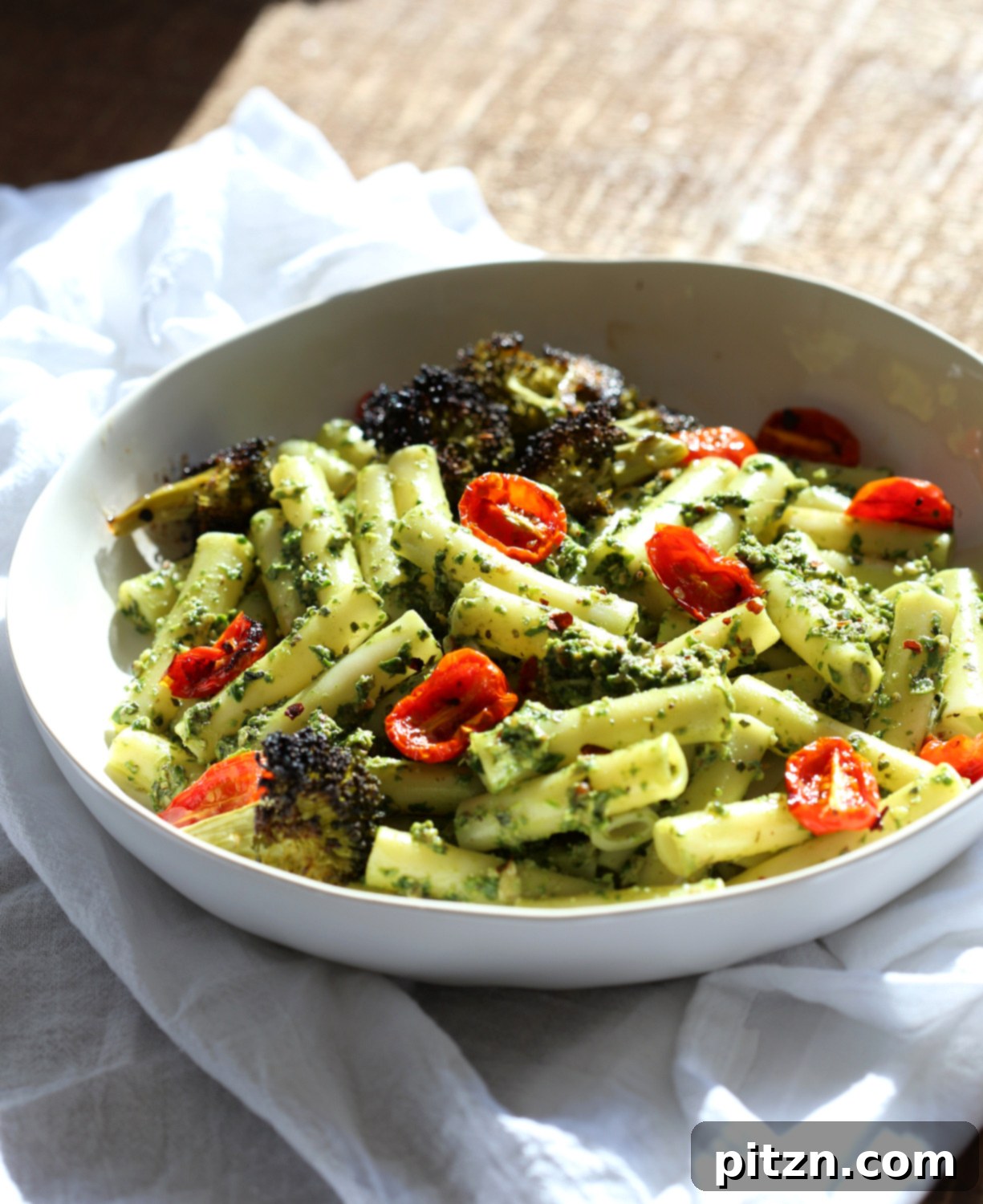 Vibrant Vegan Pesto Pasta with Smoky Charred Broccoli 3 Large white bowl with Vegan Pesto Pasta with Ziti, roasted cherry tomatoes, and broccoli on a rustic wood table.