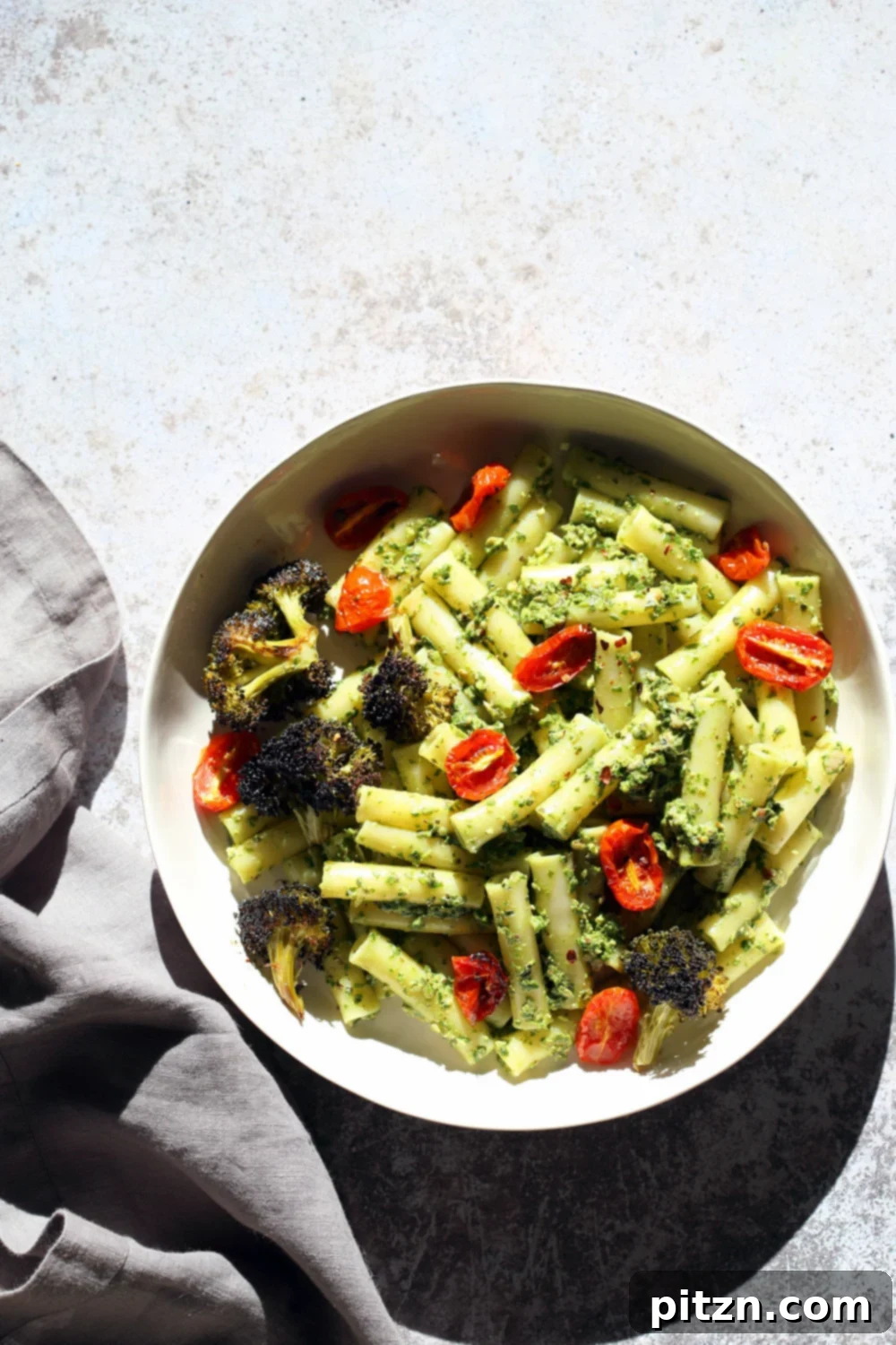 Vibrant Vegan Pesto Pasta with Smoky Charred Broccoli 8 A large serving bowl featuring Vegan Pesto Pasta with Ziti, roasted cherry tomatoes, and charred broccoli, highlighting the dish's vibrant colors and textures. This dish offers 22 grams of protein per serving and is naturally vegan and soy-free, with options for gluten-free and nut-free dietary needs.