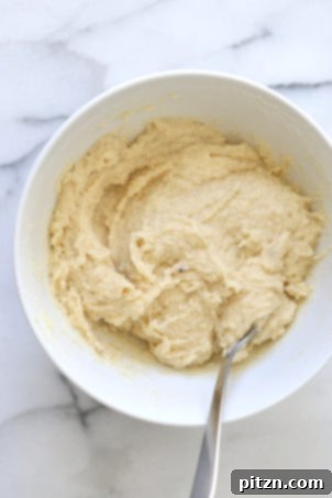 Velvety Vegan Malai Burfi Fudge 7 Combining almond flour, sugar, and cardamom in a white bowl to form the Malai Burfi mixture.