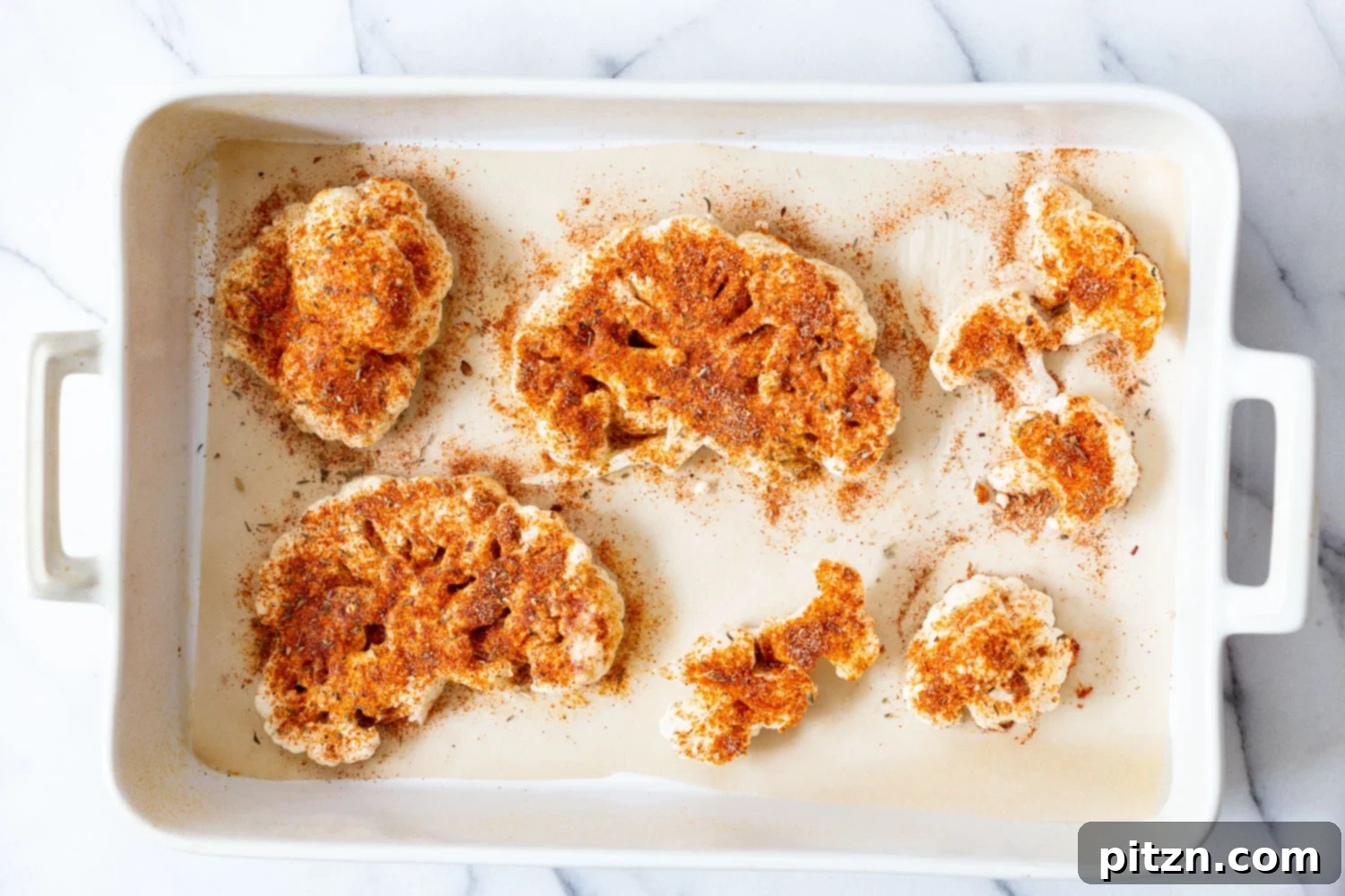 Spicy Cajun Cauliflower Steaks with Fresh Chimichurri 5 Thickly sliced cauliflower 'steaks' arranged on a parchment-lined baking dish, prepped for seasoning and roasting with Cajun spices to create a delicious vegan main.