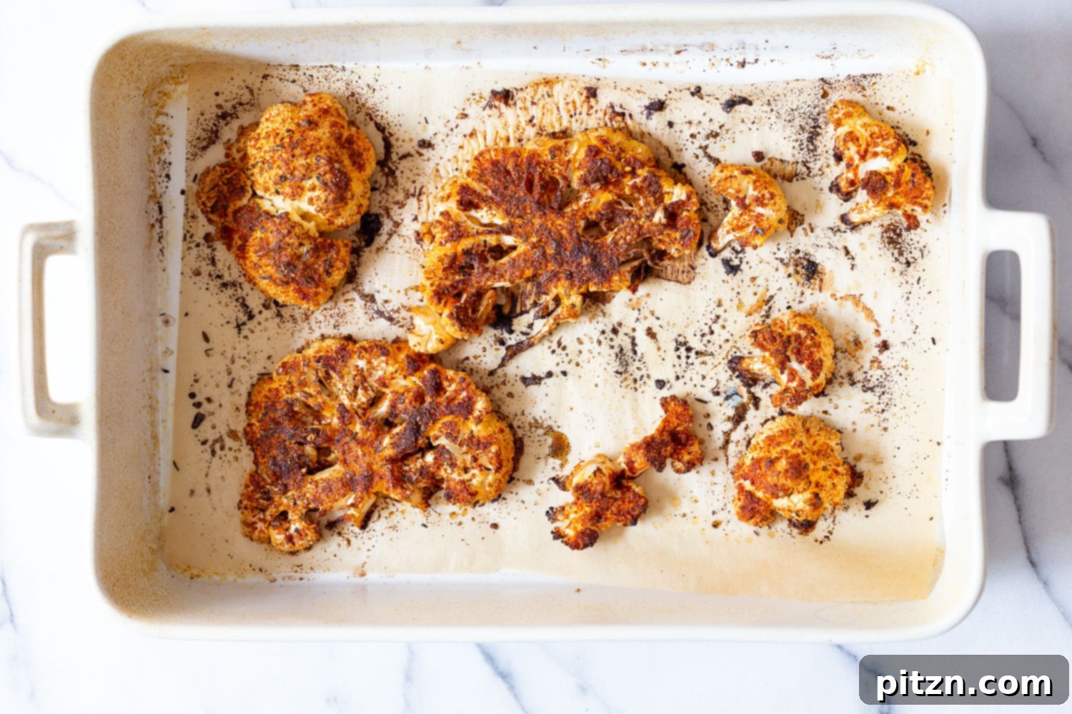 Spicy Cajun Cauliflower Steaks with Fresh Chimichurri 6 Baked Cajun Roasted Cauliflower Steaks perfectly browned and seasoned, presented on a parchment-lined white baking dish, ready to be served with fresh chimichurri.