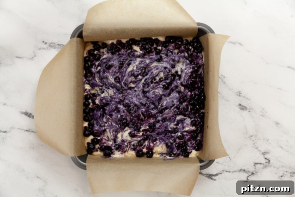 Berry Buckle Batter with blueberries in a parchment lined baking dish