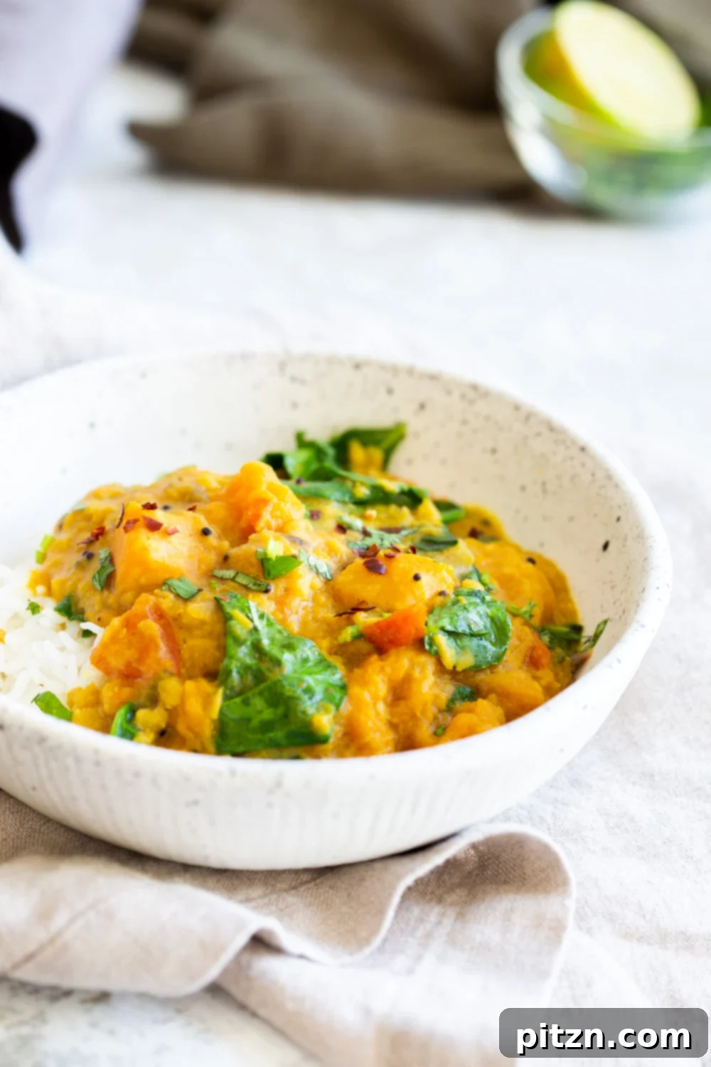 Instant Pot Red Lentil Butternut Squash Curry in a white speckled bowl kept on grey napkin