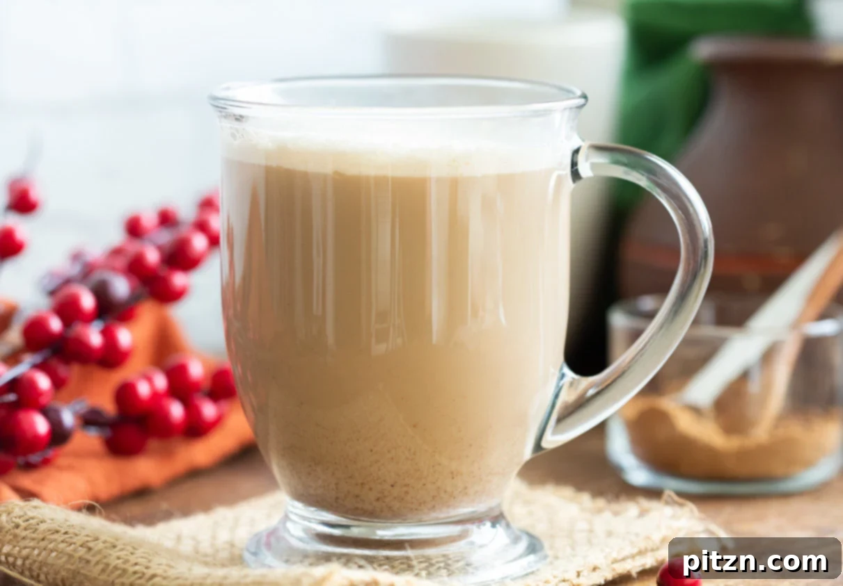 Two mugs of vegan gingerbread latte, one topped with whipped cream, photographed on a wooden surface with festive decorations.
