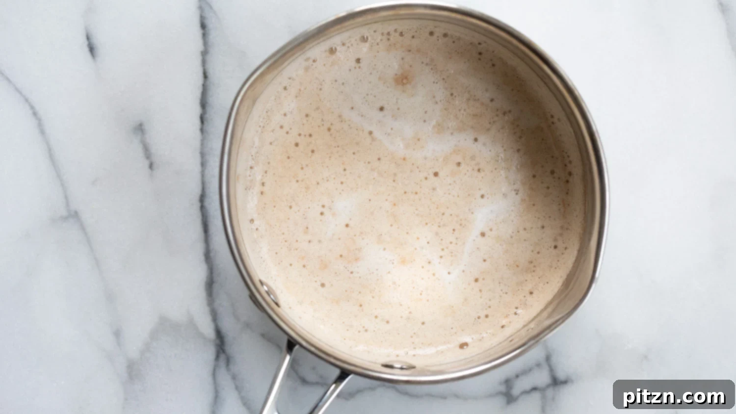 Overhead shot of a vegan gingerbread latte in a glass mug, with a cozy background of blankets and books.