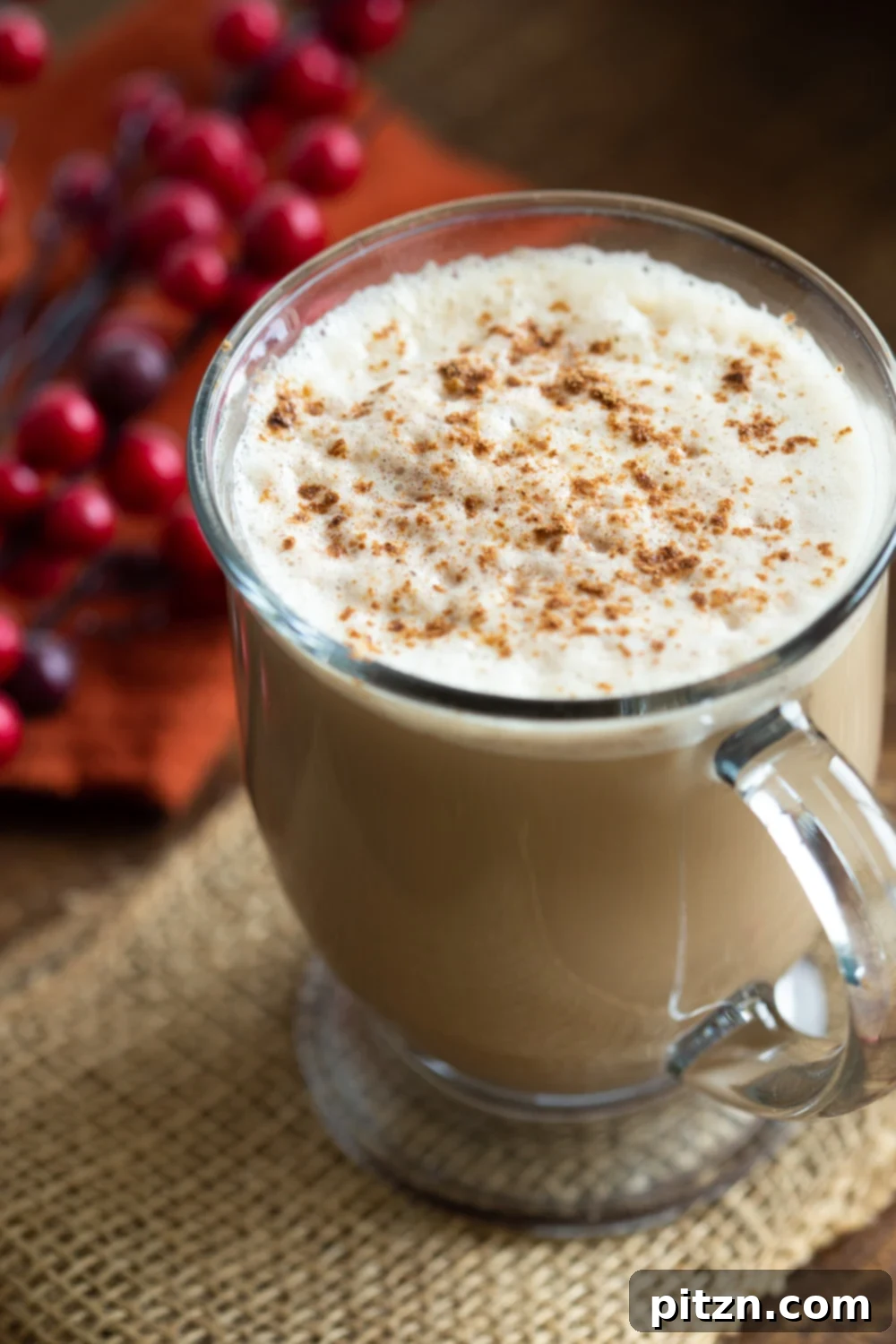 Creamy Vegan Gingerbread Latte in a clear glass mug placed on a rustic wood table, perfect for a cozy moment.