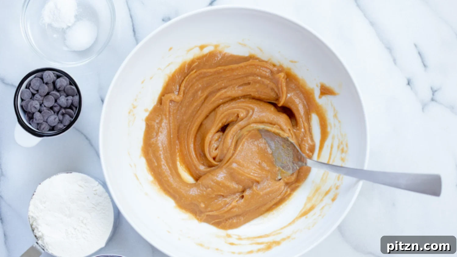 Easy One-Bowl Vegan Peanut Butter Oatmeal Chocolate Chip Cookies 5 A white bowl filled with creamy wet ingredients (peanut butter, maple syrup, milk, vanilla) for vegan cookies, after being thoroughly mixed.