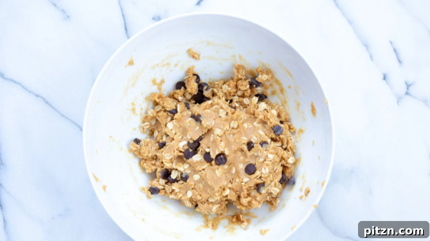 Easy One-Bowl Vegan Peanut Butter Oatmeal Chocolate Chip Cookies 7 Soft cookie dough for Vegan Peanut Butter Oatmeal Chocolate Chip Cookies in a white bowl, showing the texture before chocolate chips are added.
