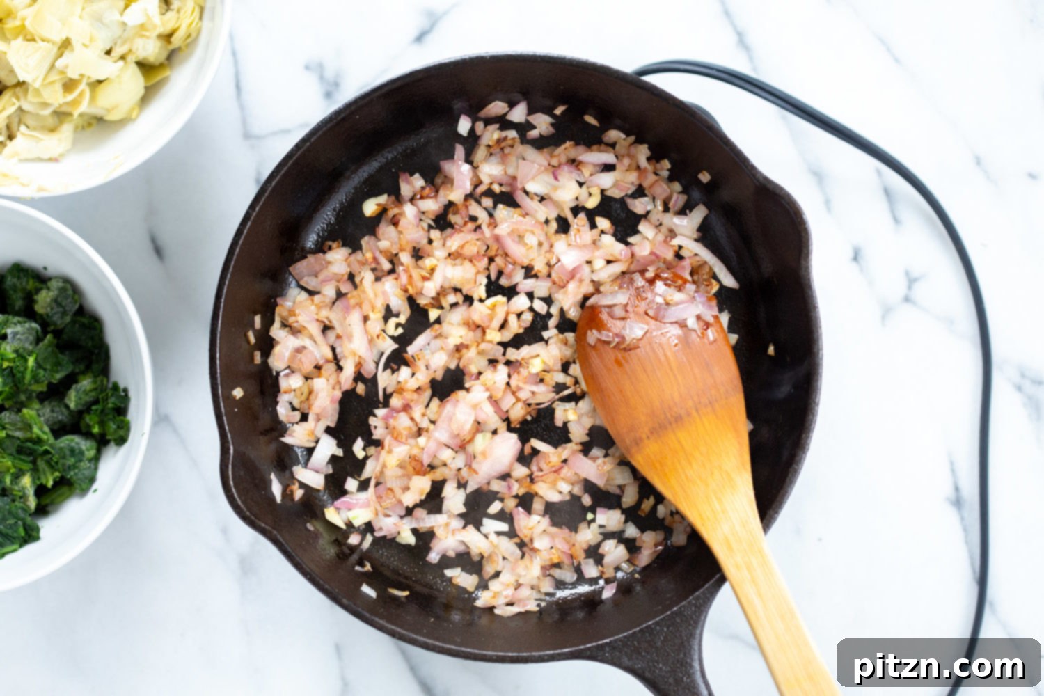 Finely chopped onion and garlic are sautéing in a hot cast iron skillet, filling the air with aromatic flavors for the dip.