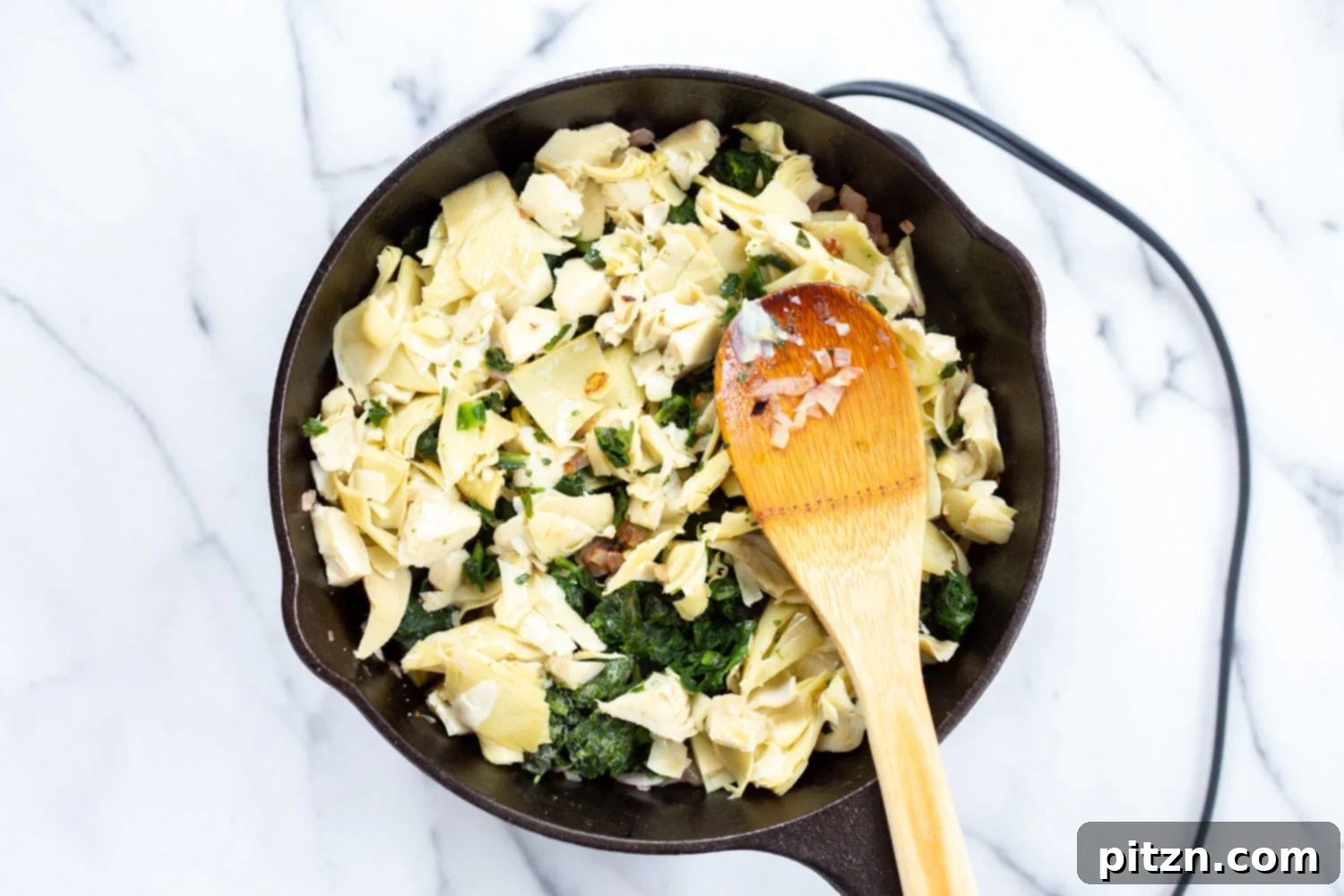 Fresh spinach and chopped artichoke hearts are cooking down in a cast iron skillet, wilting beautifully for the creamy dip.