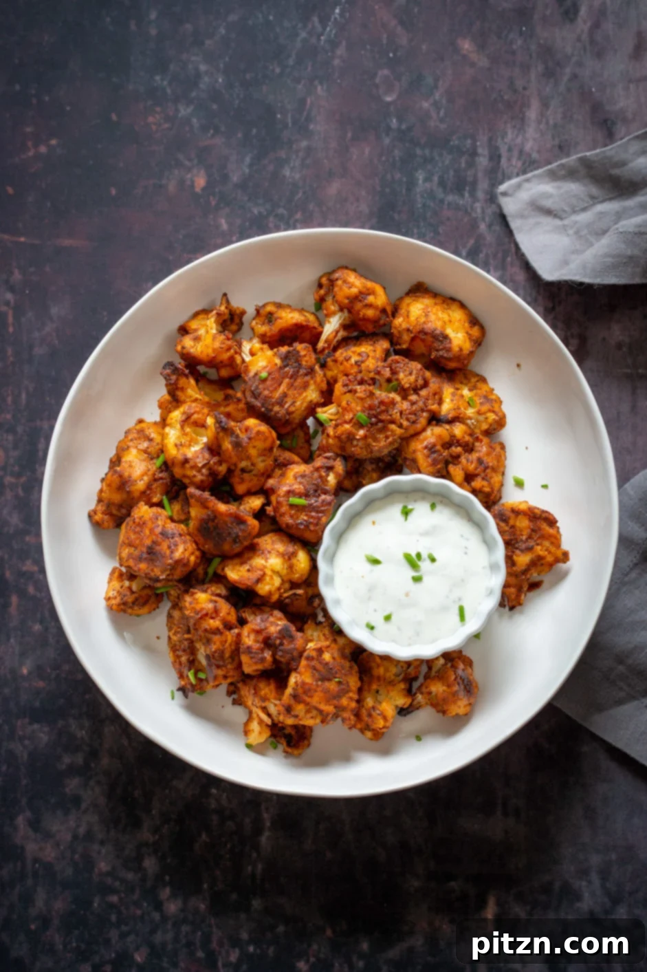 A bowl of Vegan Nashville Hot Cauliflower Wings, perfectly golden and spicy, accompanied by a side of creamy vegan ranch dip, creating a mouth-watering combination.