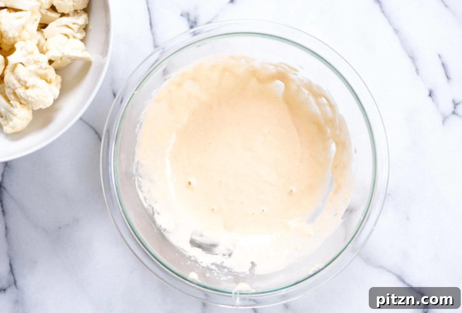 Whisk together the batter ingredients in a white bowl for your Vegan Nashville Hot Cauliflower Wings. The consistency should be thick enough to coat the florets.
