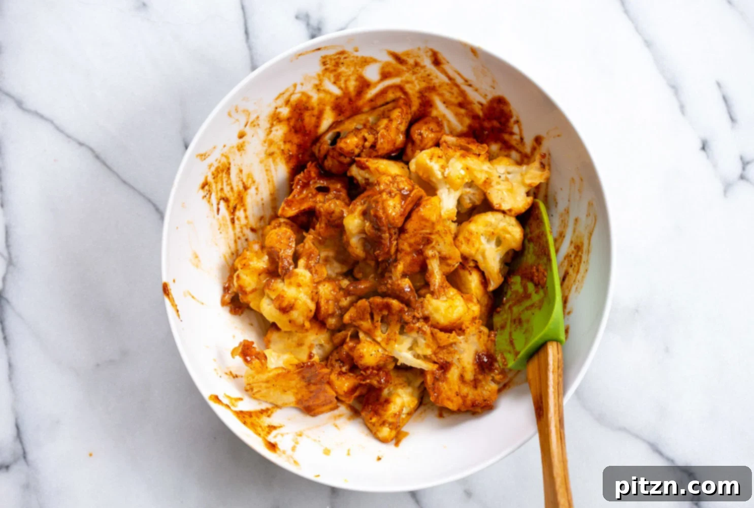 Our Baked Nashville Hot Cauliflower Wings perfectly coated with the spicy Nashville hot sauce, nestled in a white bowl, ready for their final bake.