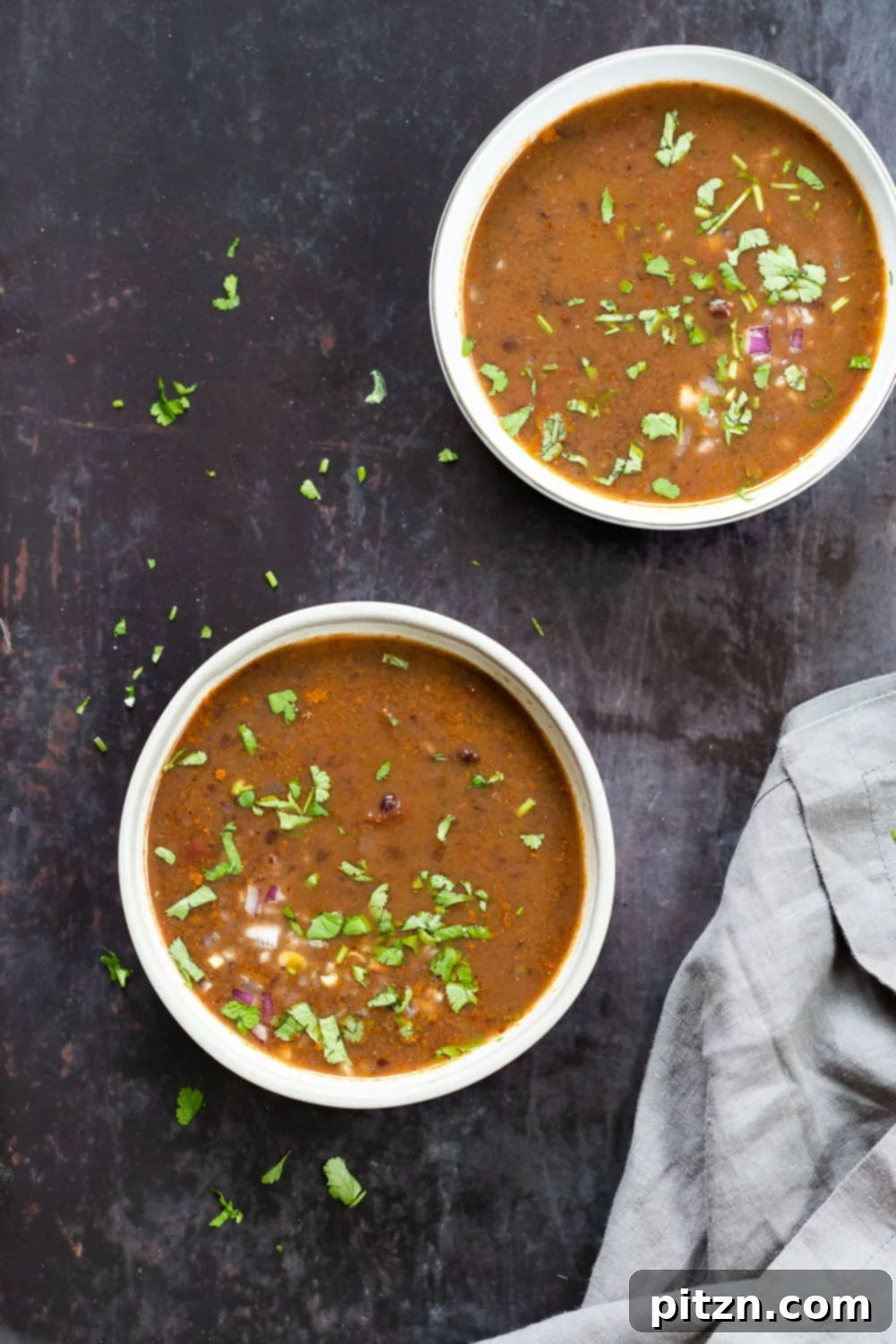 vegan black bean soup overhead shot of two bowls of vegan black beans soup sprinkled with chopped herbs