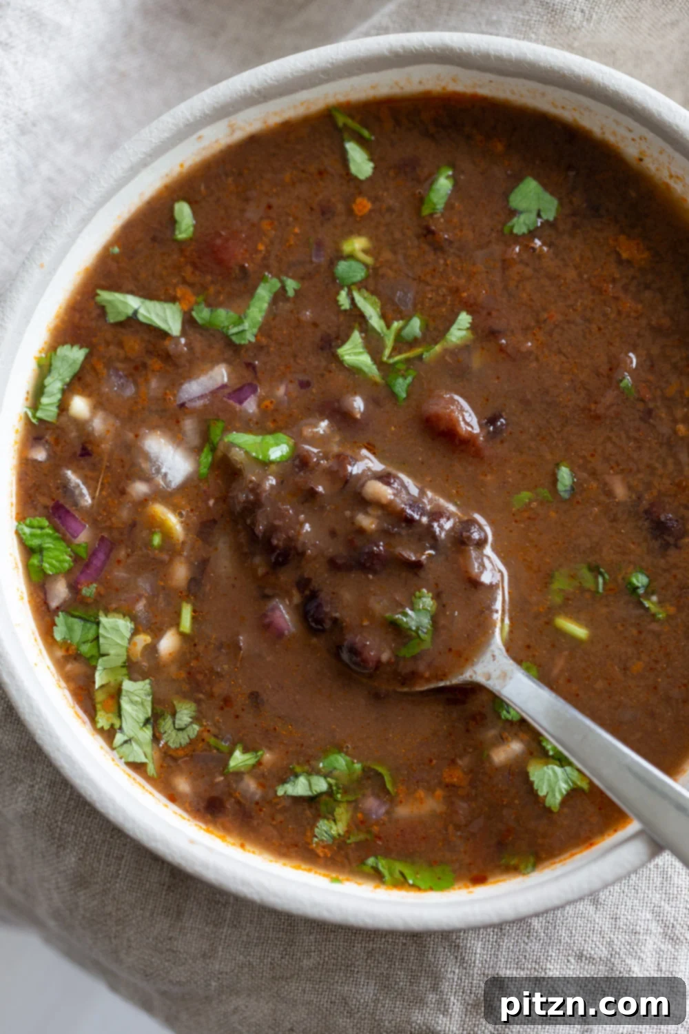 vegan black bean soup overhead shot of a white bowl with vegan black bean soup with a spoon dipping into the bowl