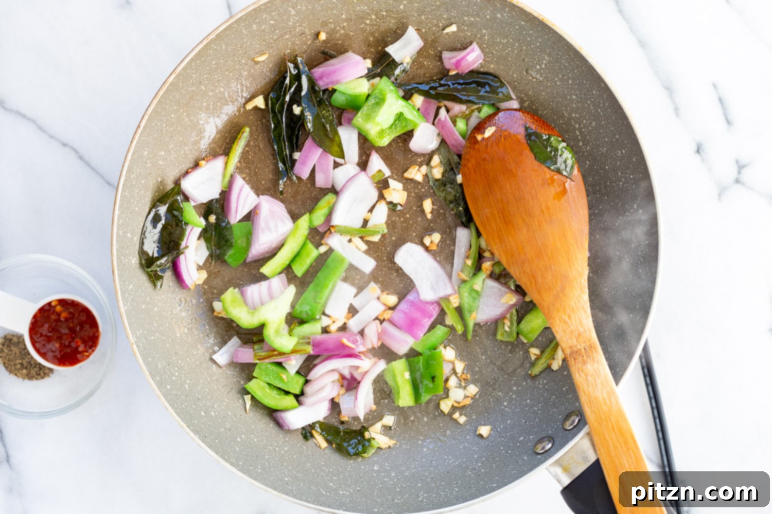 A close-up shot of the Tofu 65 sauce in a grey skillet, showcasing its rich texture and vibrant color as it thickens, infused with spices and aromatics.