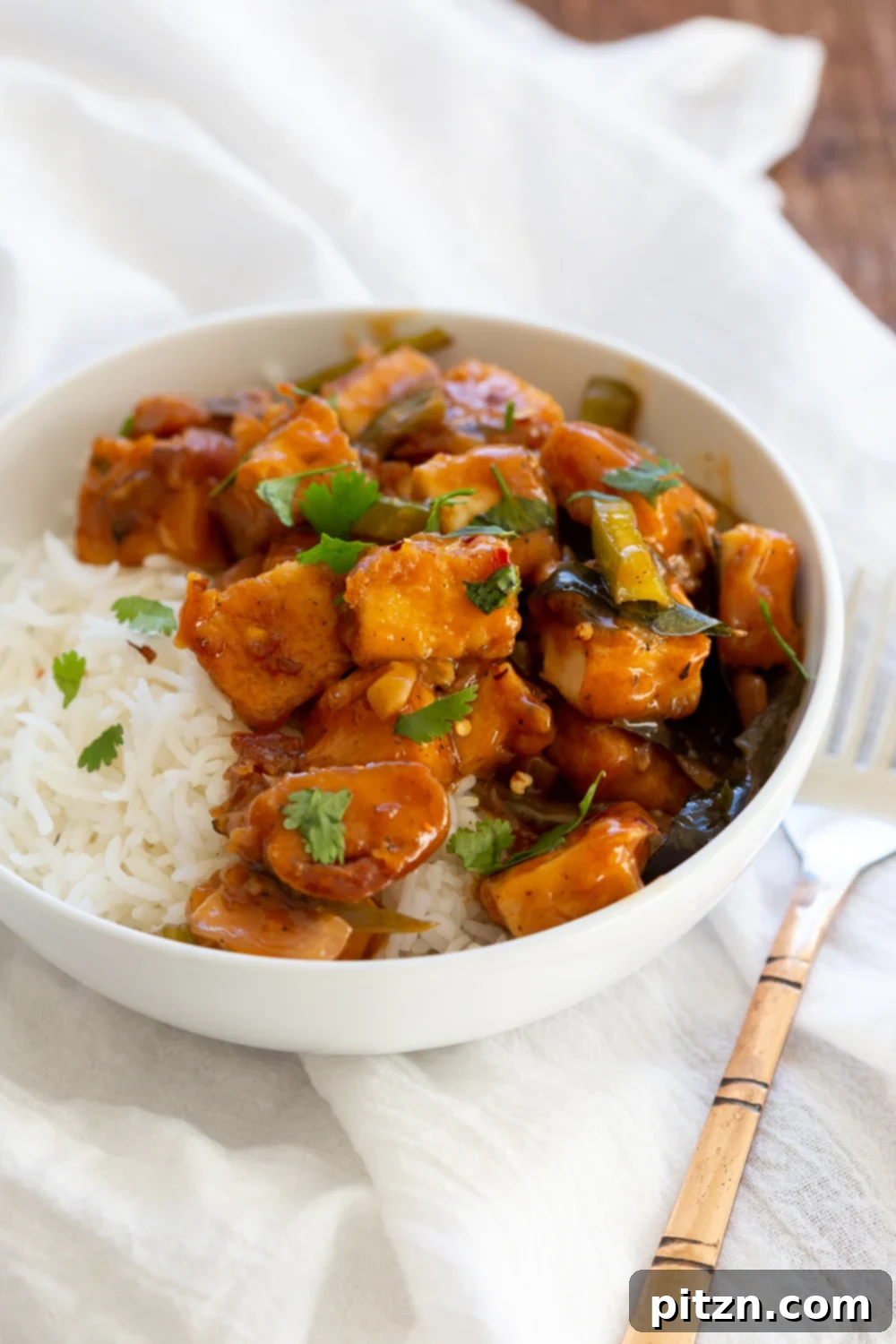 A final close-up of Tofu 65 in a white bowl, garnished with fresh cilantro, highlighting the rich sauce and crispy tofu, ready to be served.