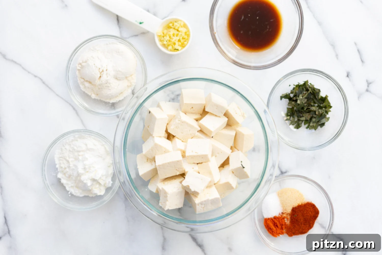 Bowls filled with the individual ingredients for Tofu 65, including pressed tofu cubes, various spices, fresh curry leaves, and chopped vegetables, ready for preparation.