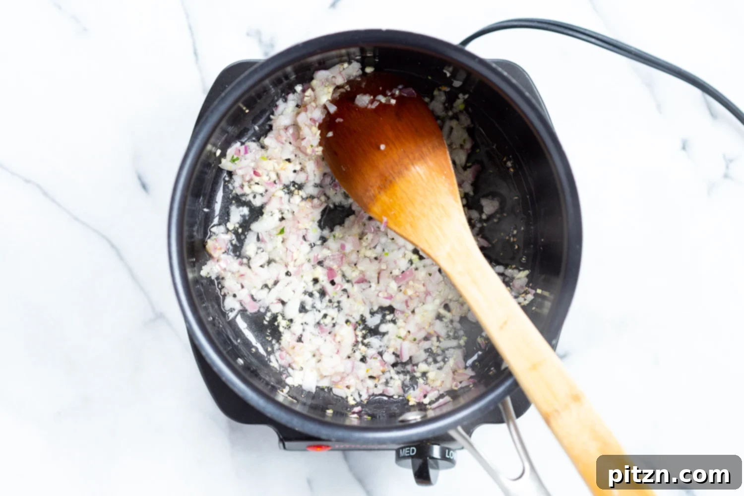 Sautéing onions and garlic for marinara sauce in a black saucepan