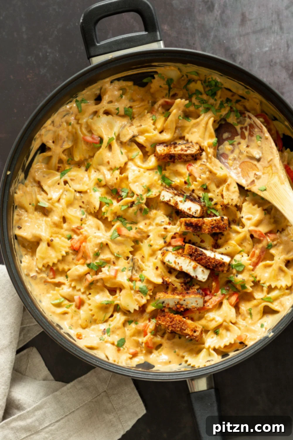 Vegan Creamy Cajun Pasta with Crisp Breaded tofu in a black skillet, garnished with fresh herbs.