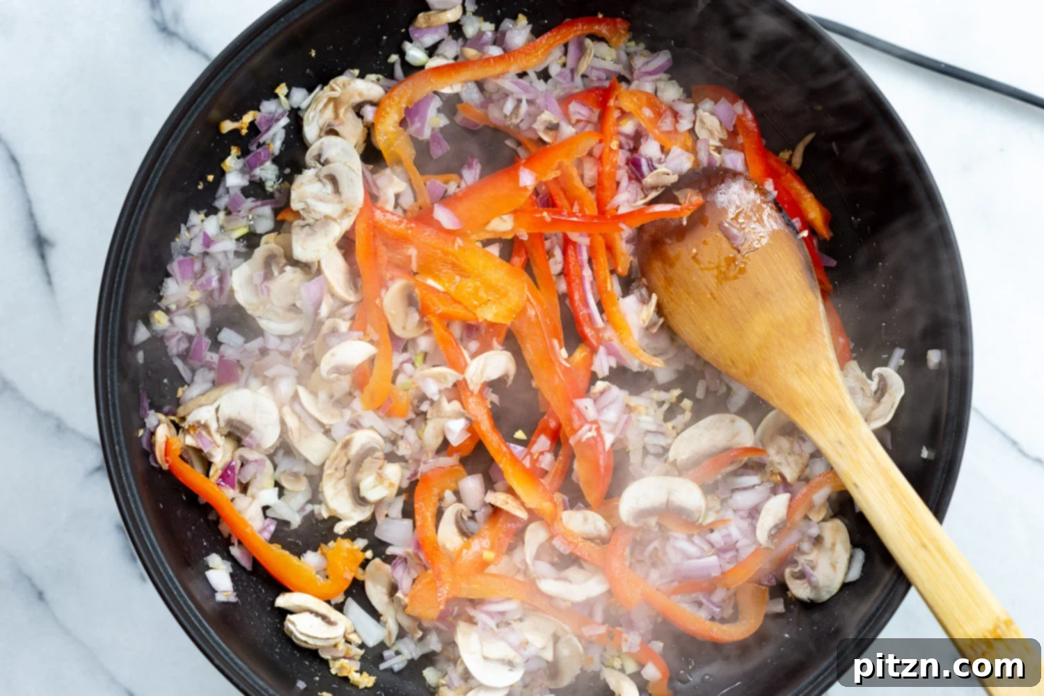 Sautéed onions and bell peppers simmering in a skillet, creating a aromatic base for the creamy Cajun pasta sauce.