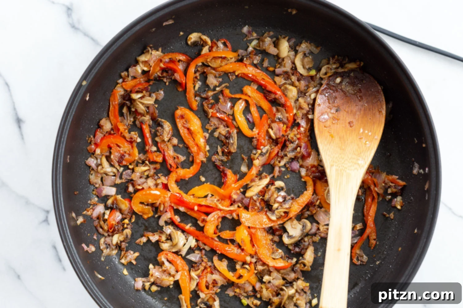 Another view of vibrant onions and bell peppers sautéing in a skillet, ready to be incorporated into the creamy Cajun pasta sauce.