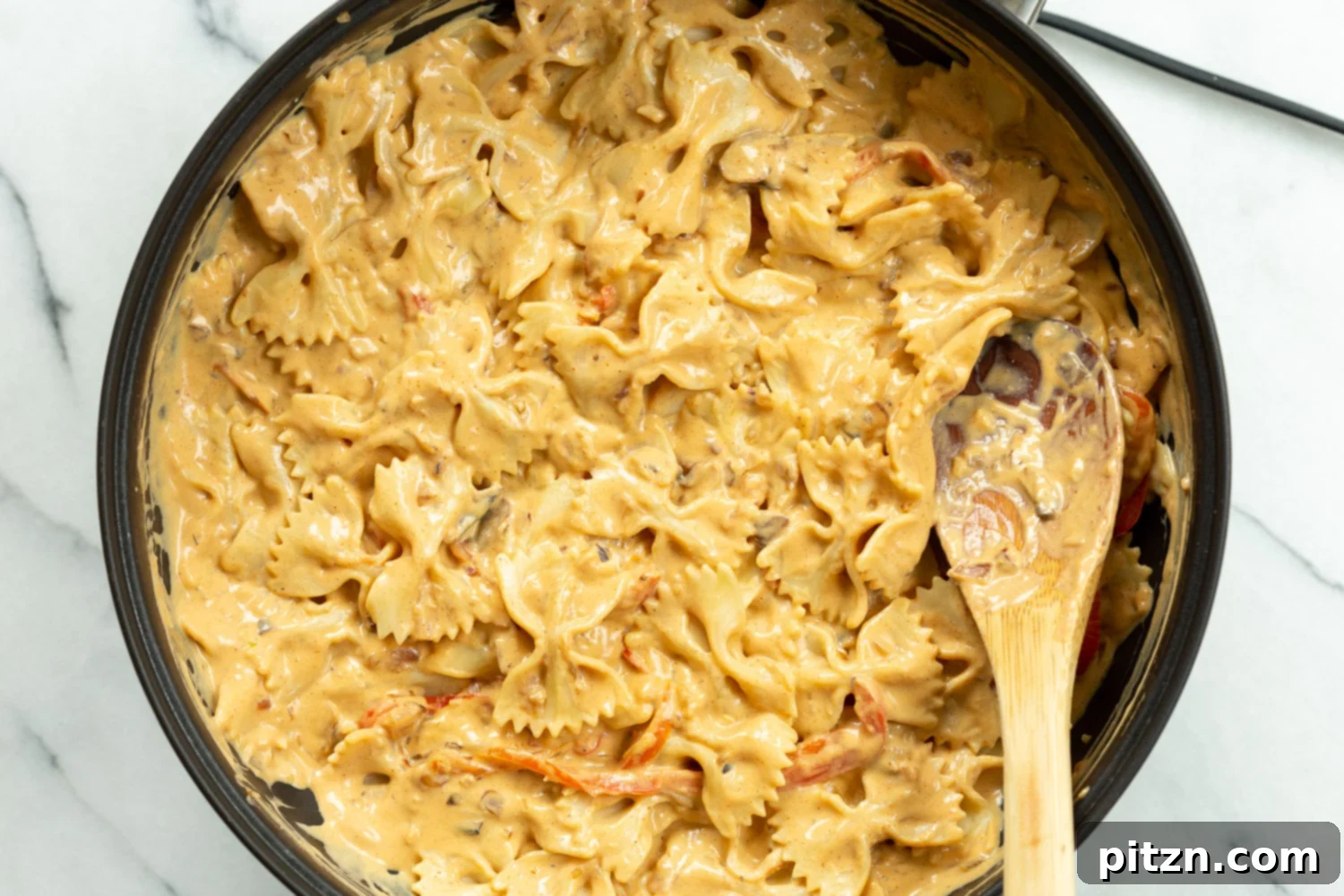 Our creamy Cajun pasta sauce mixed with farfalle pasta in a skillet, ready to be served.