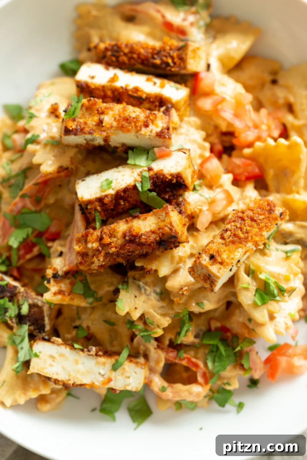 A beautifully presented serving of Vegan Creamy Cajun Pasta with Crisp Breaded tofu in a white bowl, garnished with fresh herbs.