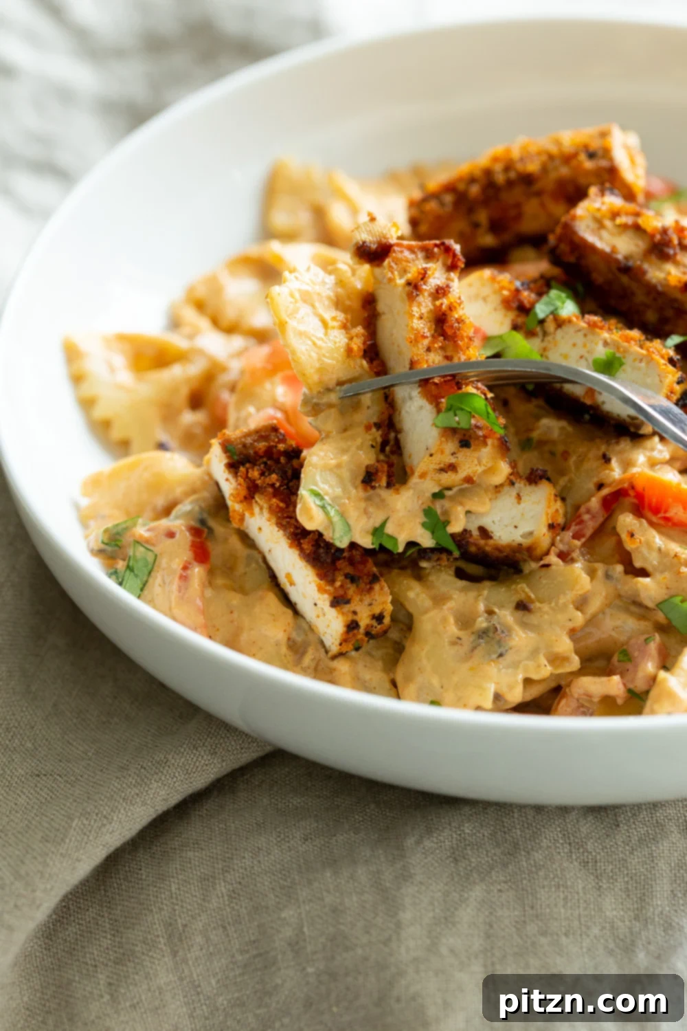 A serving of Vegan Creamy Cajun Pasta with Crisp Breaded tofu in a stylish white bowl, ready to be enjoyed.