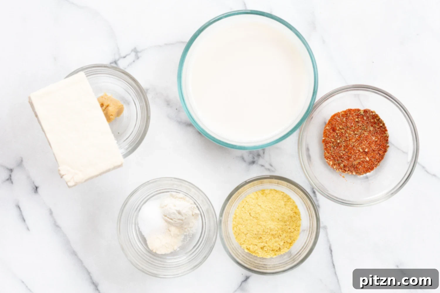 Various ingredients for the vegan creamy Cajun pasta sauce arranged in bowls, including tofu, vegetables, and spices.