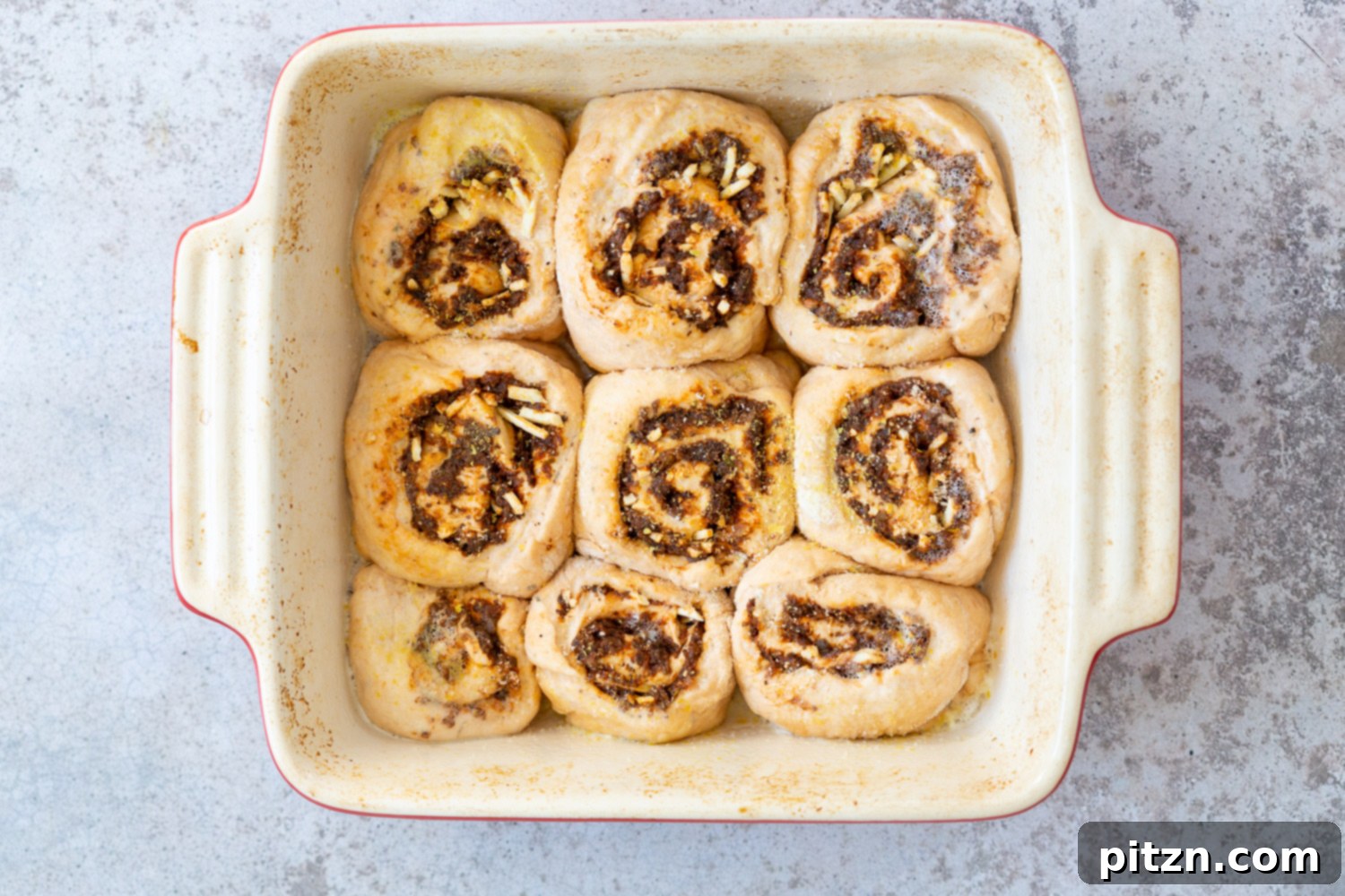 The Ultimate Vegan Pizza Rolls 13 Unbaked Vegan Pizza Rolls neatly arranged in a ceramic baking dish, ready for their final rise and baking, promising a delicious outcome.